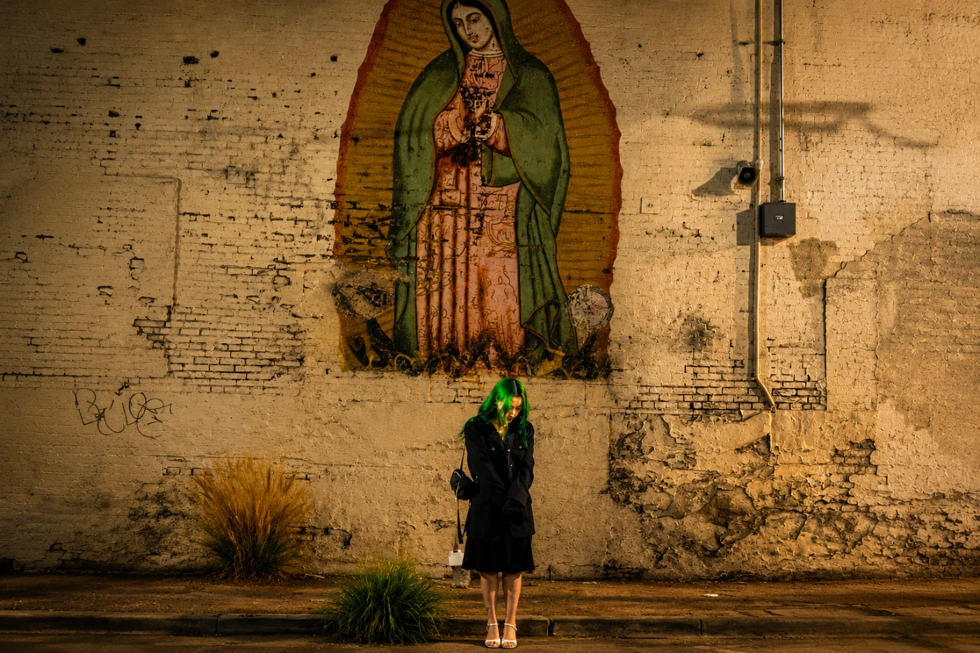 Bella standing beneath a mural of the Virgin of Guadalupe on a Los Angeles brick wall at dusk